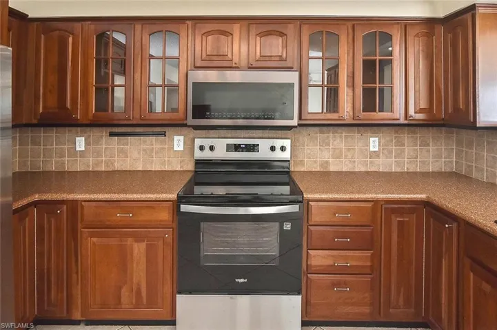 Kitchen with stainless steel appliances, glass insert cabinets, decorative backsplash, and brown cabinetry
