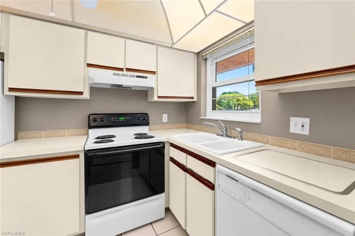 Kitchen featuring cream cabinetry, a white electric range, double basin sink, and a built-in dishwasher