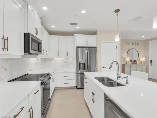 Kitchen with white cabinets, appliances with stainless steel finishes, sink, pendant lighting, and decorative backsplash