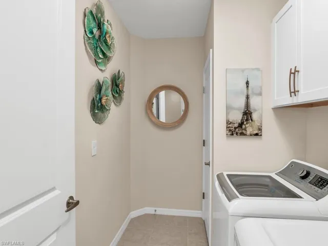 Washroom with light tile patterned flooring, cabinets, and washing machine and dryer
