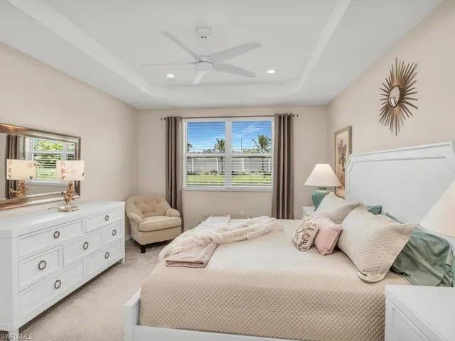 Bedroom featuring a tray ceiling, multiple windows, light colored carpet, and ceiling fan