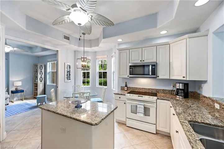 Kitchen featuring a tray ceiling, a ceiling fan, white electric stove, light stone counters, and stainless steel microwave