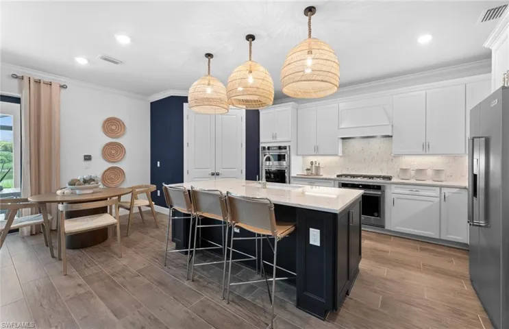 Kitchen with crown molding, a kitchen island with sink, a kitchen breakfast bar, light stone countertops, and stainless steel appliances
