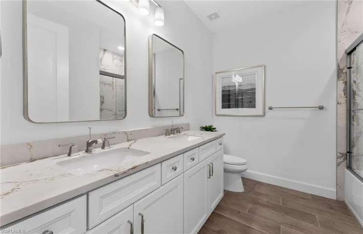 Bathroom featuring double vanity, wood finish floors, and shower / bath combination with glass door