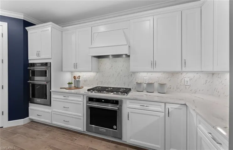 Kitchen with crown molding, stainless steel appliances, white cabinets, wood finish floors, and light stone counters