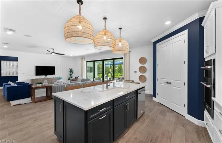 Kitchen featuring open floor plan, dark cabinetry, wood tiled floors, light stone counters, and ornamental molding