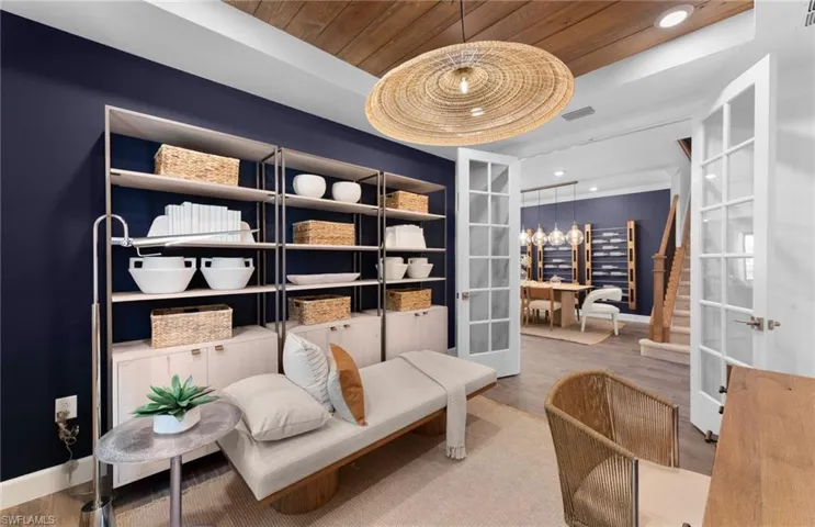 Living area featuring light wood finished floors, a wood tray ceiling, suspended lighting, and french doors