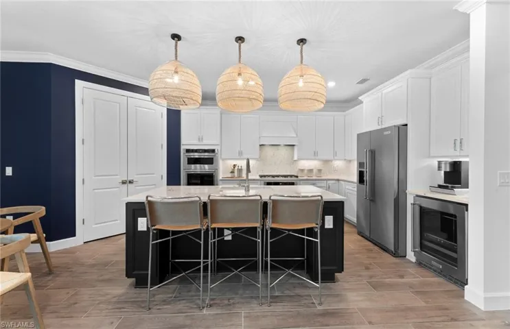 Kitchen with a kitchen bar, a kitchen island with sink, wood finish floors, stainless steel appliances, and tasteful backsplash