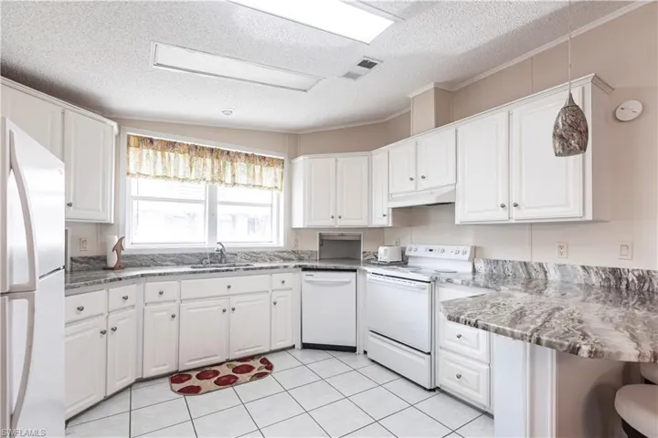 Kitchen featuring a sink, under cabinet range hood, white appliances, visible vents, and white cabinets