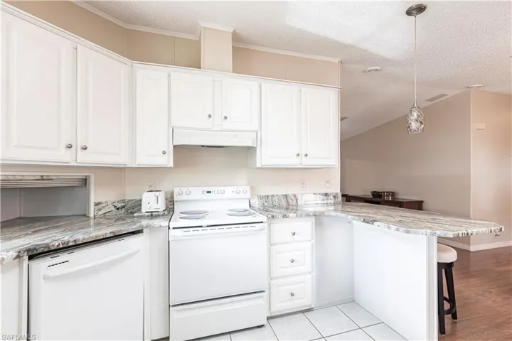 Kitchen featuring a peninsula, white appliances, under cabinet range hood, white cabinetry, and a breakfast bar area