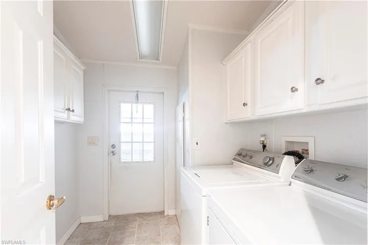 Washroom with a textured ceiling, baseboards, washer and clothes dryer, cabinet space, and light tile patterned floors