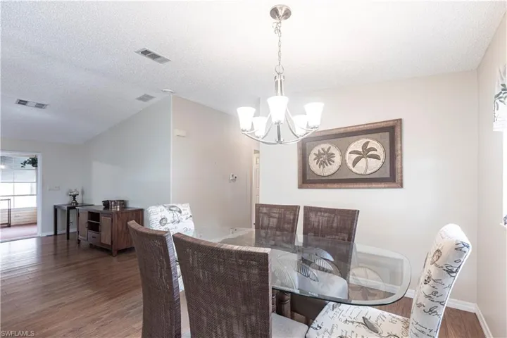 Dining room with visible vents, a notable chandelier, wood finished floors, and a textured ceiling