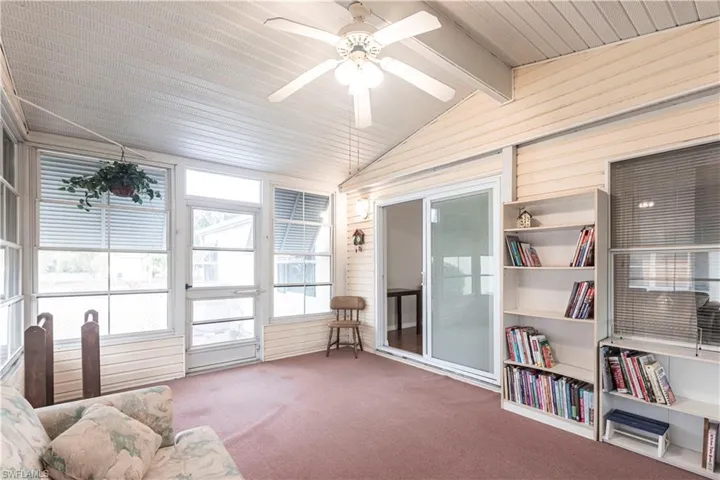 Sunroom / solarium featuring carpet flooring, a ceiling fan, lofted ceiling with beams, and wooden walls