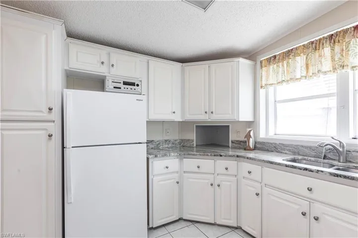 Kitchen featuring freestanding refrigerator, white cabinets, a sink, and light stone countertops