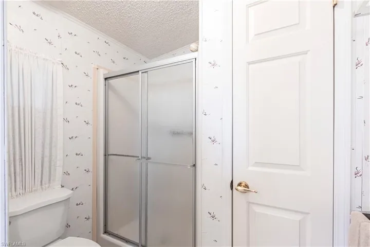 Bathroom featuring a textured ceiling, toilet, a shower stall, and wallpapered walls