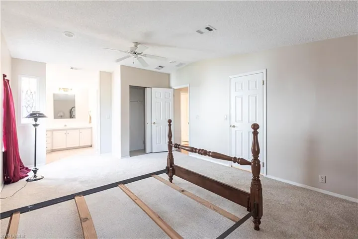 Bedroom with light carpet, a textured ceiling, ensuite bathroom, and visible vents