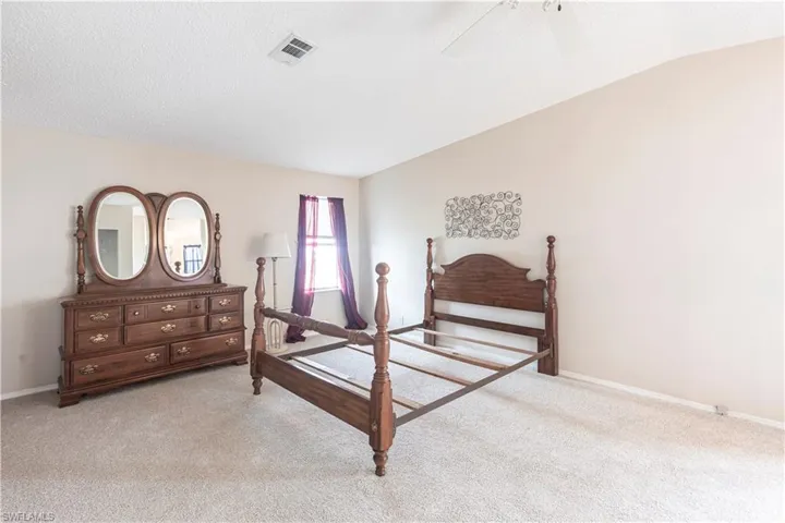Bedroom with a textured ceiling, visible vents, baseboards, ceiling fan, and light carpet