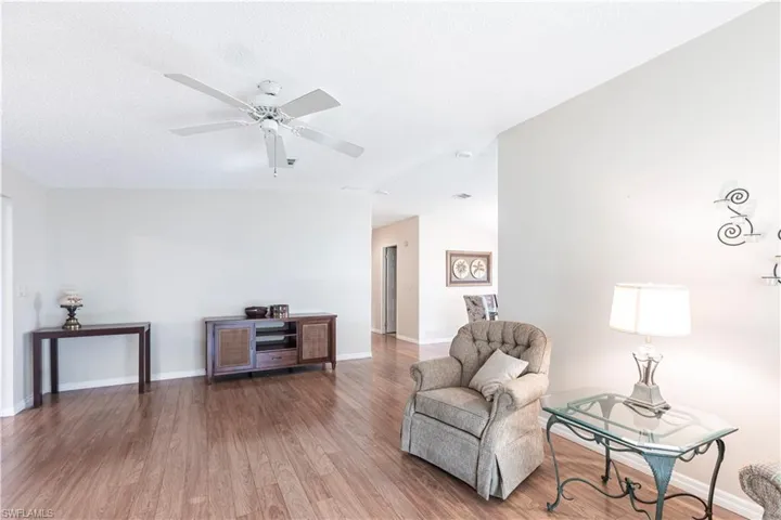 Living area with a textured ceiling, baseboards, wood finished floors, a ceiling fan, and vaulted ceiling