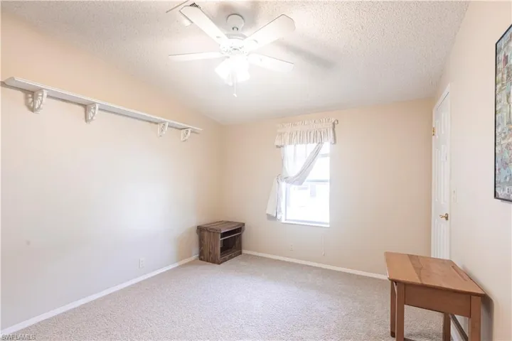 Carpeted spare room featuring a textured ceiling, lofted ceiling, ceiling fan, and baseboards