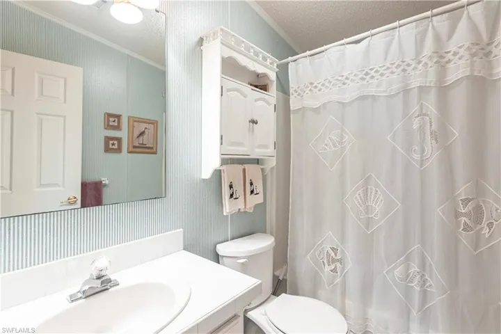 Bathroom with toilet, curtained shower, vanity, a textured ceiling, and ornamental molding