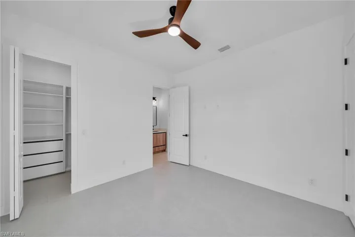 Unfurnished bedroom with a spacious closet, a ceiling fan, finished concrete floors, and ensuite bathroom