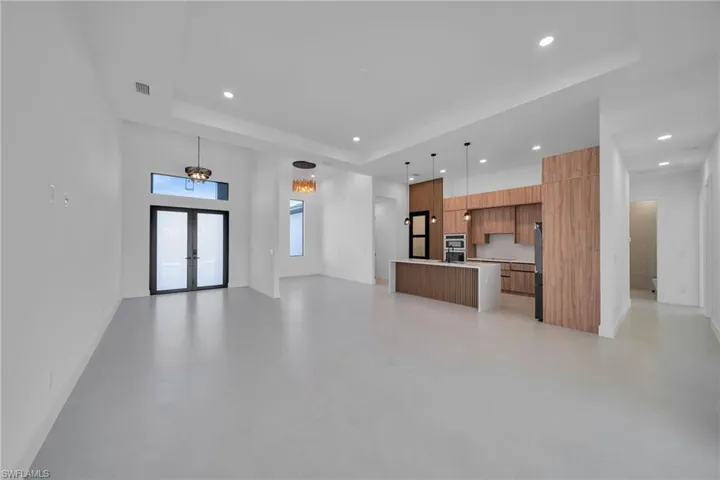 Unfurnished living room featuring french doors, a raised ceiling, finished concrete floors, and recessed lighting