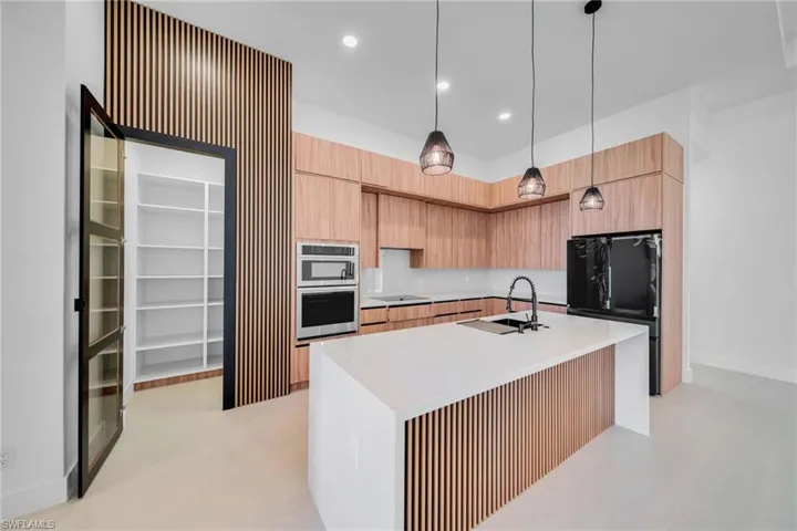 Kitchen with an island with sink, black appliances, modern cabinets, and pendant lighting