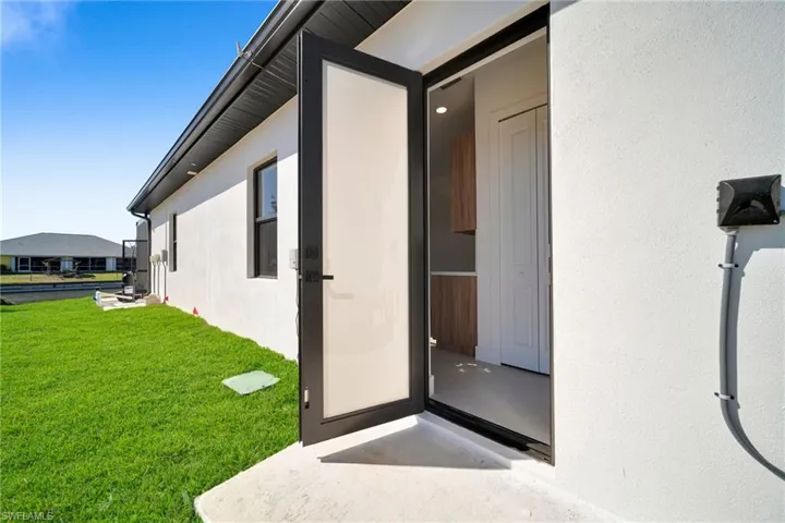 View of exterior entry with stucco siding and a lawn