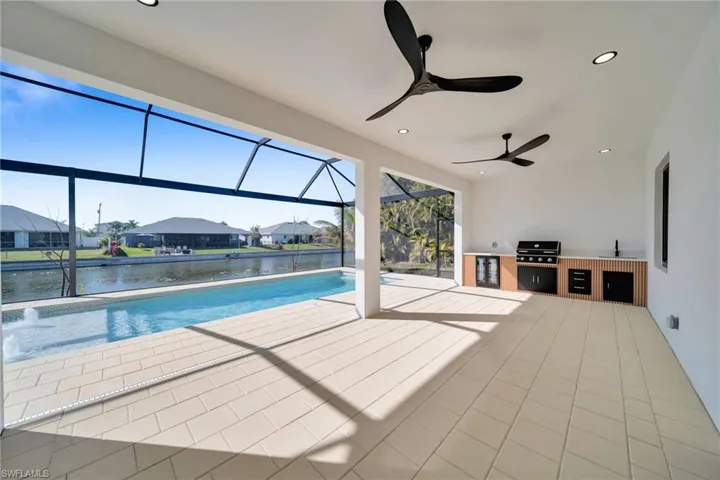 Swimming pool with a sunroom, a residential view, a patio area, exterior kitchen, and glass enclosure