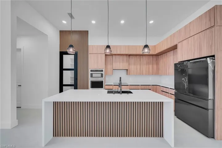 Kitchen with black appliances, a kitchen island with sink, light stone counters, modern cabinets, and decorative light fixtures