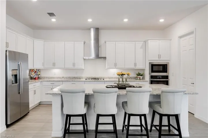 Kitchen featuring white cabinets, an island with sink, appliances with stainless steel finishes, and wall chimney range hood