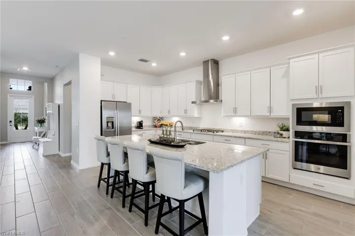 Kitchen with white cabinets, a center island with sink, stainless steel appliances, and wall chimney range hood