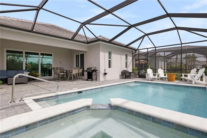 View of pool with a grill, glass enclosure, an in ground hot tub, and a patio area