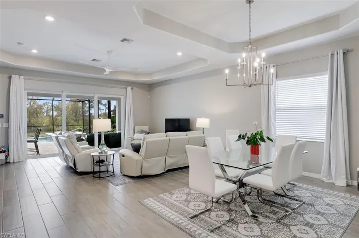 Dining area with ceiling fan with notable chandelier, light wood-type flooring, and a tray ceiling