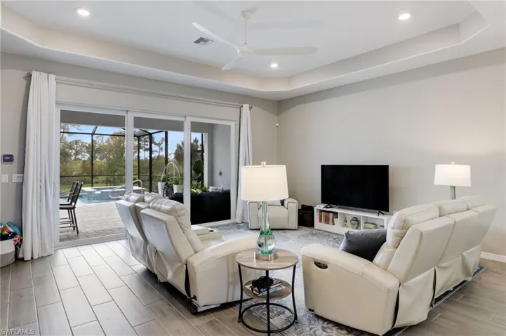 Living room featuring light wood-type flooring, a raised ceiling, and ceiling fan