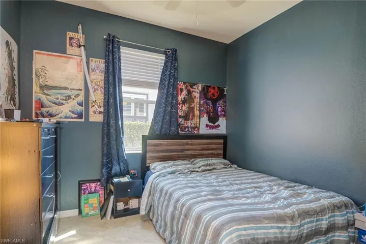 Bedroom featuring a window with blinds and patterned curtains, a textured accent wall, and ceiling fan