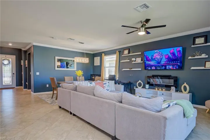 Open-concept living space featuring neutral tile flooring, a ceiling fan, and a dining area with a linear chandelier