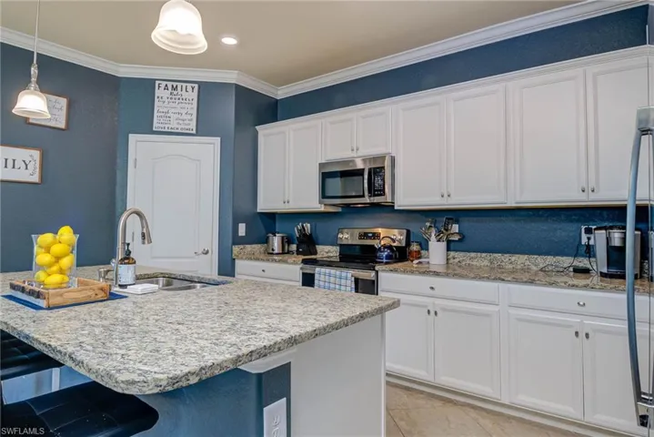 Kitchen featuring an island with a built-in sink, stainless steel gooseneck faucet, light-toned speckled countertops, white cabinetry, and recessed lighting