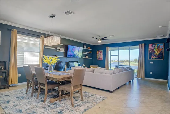 Open-concept living space with tile flooring throughout, featuring a dining area with a linear chandelier, built-in shelving, and a screened lanai with outdoor scenery