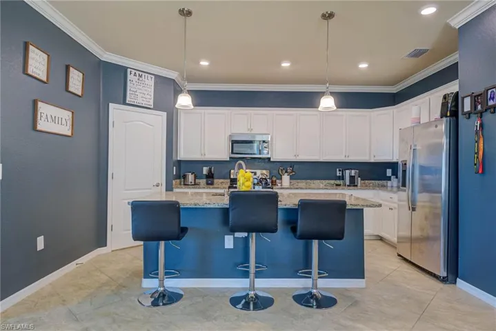 Kitchen featuring white cabinetry, granite countertops, stainless steel appliances, and a central island with pendant lighting