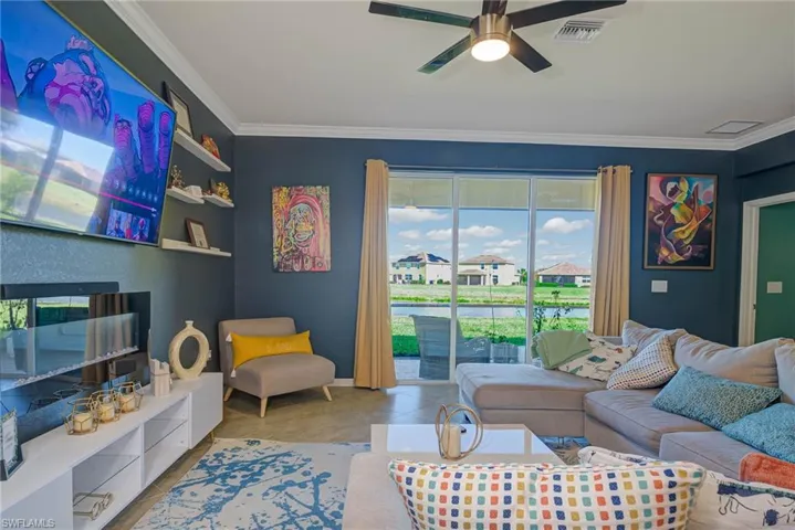 Open-concept living space with expansive sliding glass doors, a ceiling fan, crown molding, and a water feature beyond the patio