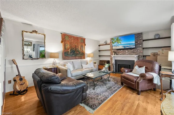 Living room with brick wall, a brick fireplace, a textured ceiling, and light wood-type flooring