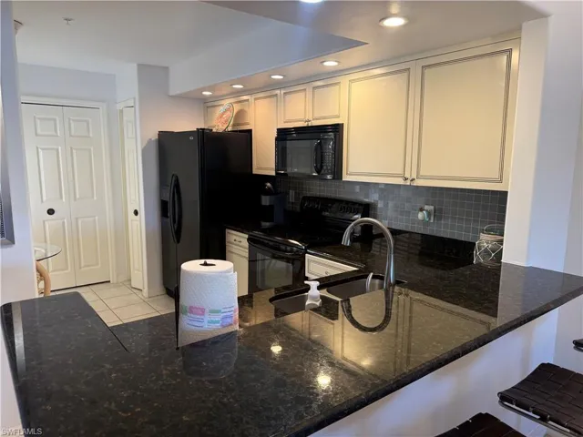 Kitchen with black appliances, dark stone countertops, a peninsula, a kitchen breakfast bar, and recessed lighting