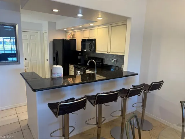 Kitchen with a breakfast bar area, black appliances, a peninsula, dark stone countertops, and light tile patterned flooring