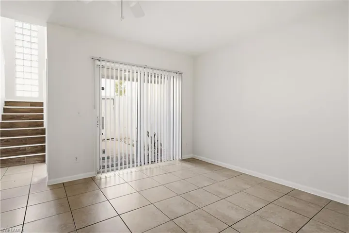 Spacious room featuring neutral tile flooring, light walls, and a sliding glass door with vertical blinds