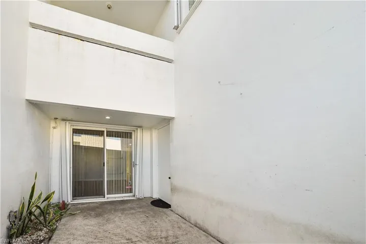 Ground level concrete patio with a sliding glass door entry, overhead recessed lighting, and a small planter bed with foliage