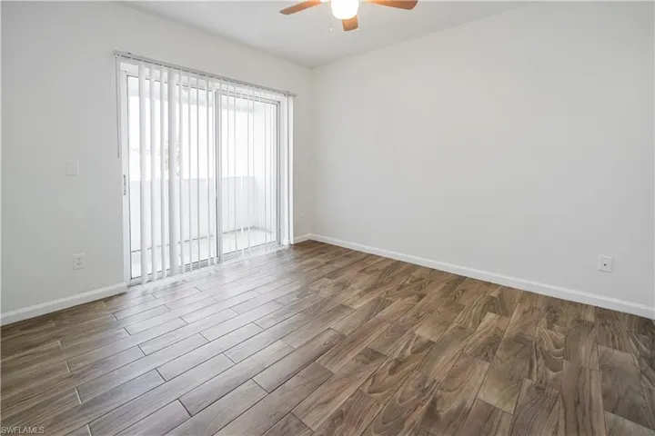 Room featuring wood-finish flooring, a ceiling fan with integrated lighting, and a sliding glass door with vertical blinds opening to an exterior space