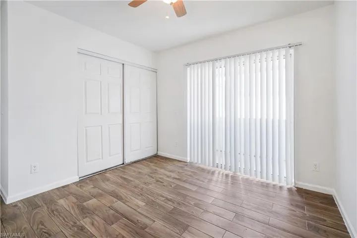 Room featuring wood-finish flooring, white vertical blinds, a ceiling fan, and sliding closet doors