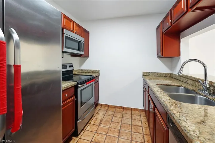 Kitchen featuring stainless steel appliances, rich wood cabinetry, granite countertops, and tile flooring