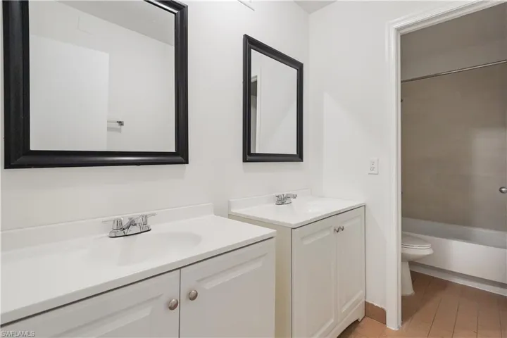 Dual-vanity bathroom featuring white cabinetry with hardware accents, white quartz countertops, and framed black mirrors